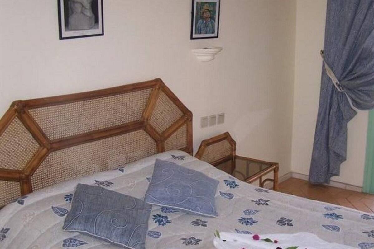A bedroom with a wooden headboard, a bed with a floral bedspread, a small bedside table, and a wall-mounted shelf.