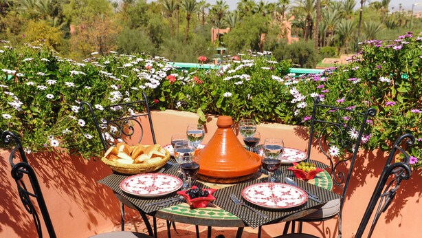 An outdoor dining area with a table set for two, surrounded by lush greenery and flowers. - In Club Palmeraie Resort (Marrakech)