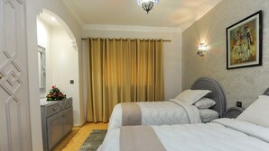 A hotel room with two beds, a grey cabinet, a decorative mirror, a painting on the wall, and a window with curtains. - In Club Palmeraie Resort (Marrakech)