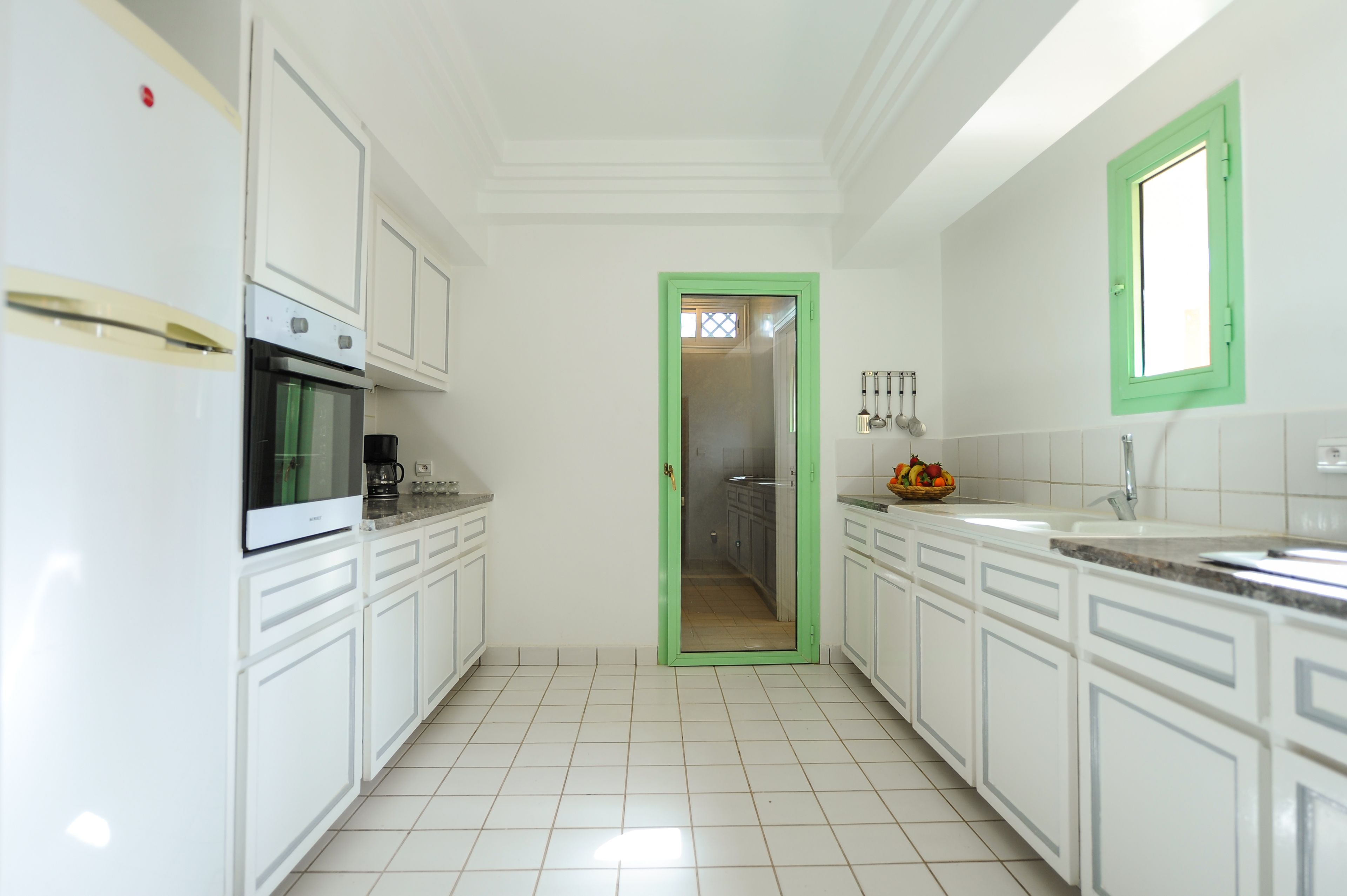 Una cocina moderna con armarios blancos, un refrigerador de acero inoxidable, un horno empotrado y un vano con marco verde que da a otra habitación.