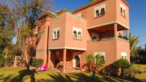 A multi-story building with balconies, a patio area with seating, and lush landscaping. - In Club Palmeraie Resort (Marrakech)
