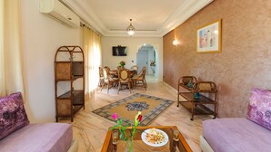 A living room with a dining area, a television mounted on the wall, and a patterned rug on the floor. - In Club Palmeraie Resort (Marrakech)