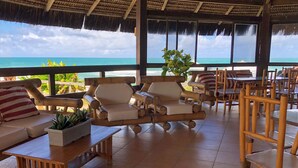 A covered outdoor seating area with bamboo furniture, potted plants, and a view of the ocean. - Armacao Hotel Porto de Galinhas (Porto Des Galinhas)