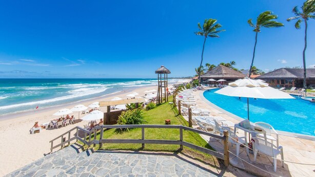 A beachside resort with a swimming pool, lounge chairs, and a thatched-roof gazebo. - Armacao Hotel Porto de Galinhas (Porto Des Galinhas)