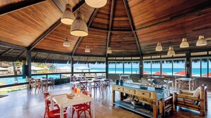 A spacious dining area with a wooden ceiling, large windows overlooking the beach, and a central island with seating. - Armacao Hotel Porto de Galinhas (Porto Des Galinhas)