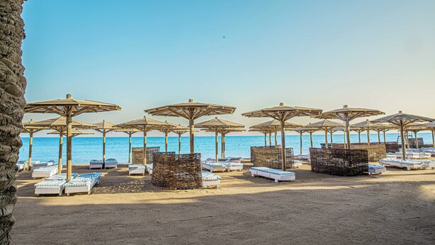 A beach with rows of sunbeds and umbrellas, a clear sky, and the sea in the background. - Eurotel Palm Beach Resort (Hurghada)
