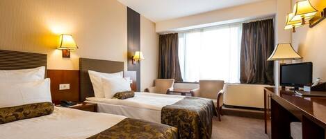 A hotel room with two beds, a desk, a chair, a TV, and a window with curtains.