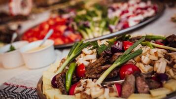 A platter of grilled meat and vegetables, including tomatoes and onions, on a table.