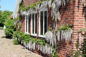 A brick building with white-framed windows and hanging white flowers. - Colston Hall Cottages (Woodbridge)