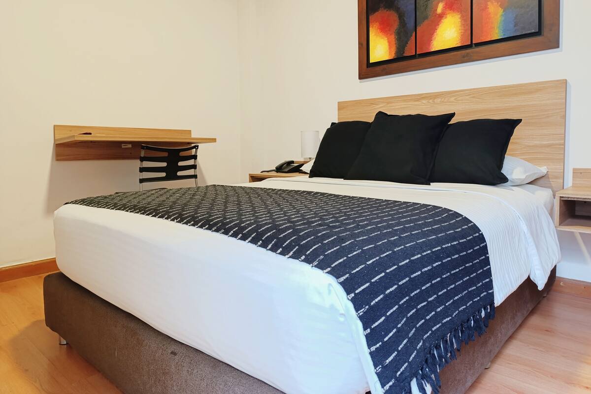 A neatly arranged bedroom with a bed, bedside table, and a small desk with a chair.