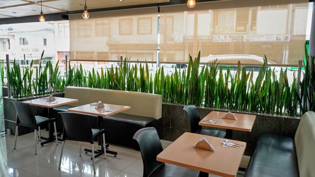 A restaurant with tables and booths, green plants, and a city view. - Hotel Volare (Armenia)
