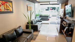 A modern living room with a black leather sofa, a glass coffee table, and a large painting on the wall. - Hotel Volare (Armenia)