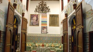 A traditional Moroccan interior with a green sofa set, a chandelier, and intricate tile work on the walls. - Riad El Bacha (Fes)