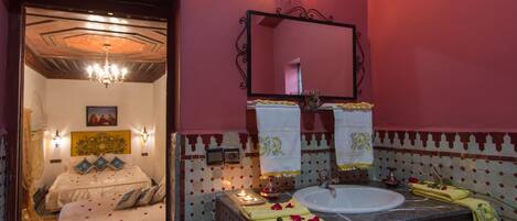 A hotel room with a bed, a bathroom with a sink and mirror, and decorative elements like candles and towels.