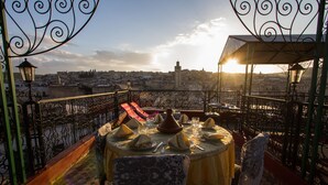 A terrace with a table set for two, overlooking a cityscape with a prominent tower. - Riad El Bacha (Fes)