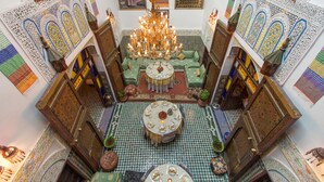 A traditional Moroccan interior with ornate tile work, a central chandelier, and a round dining table. - Riad El Bacha (Fes)