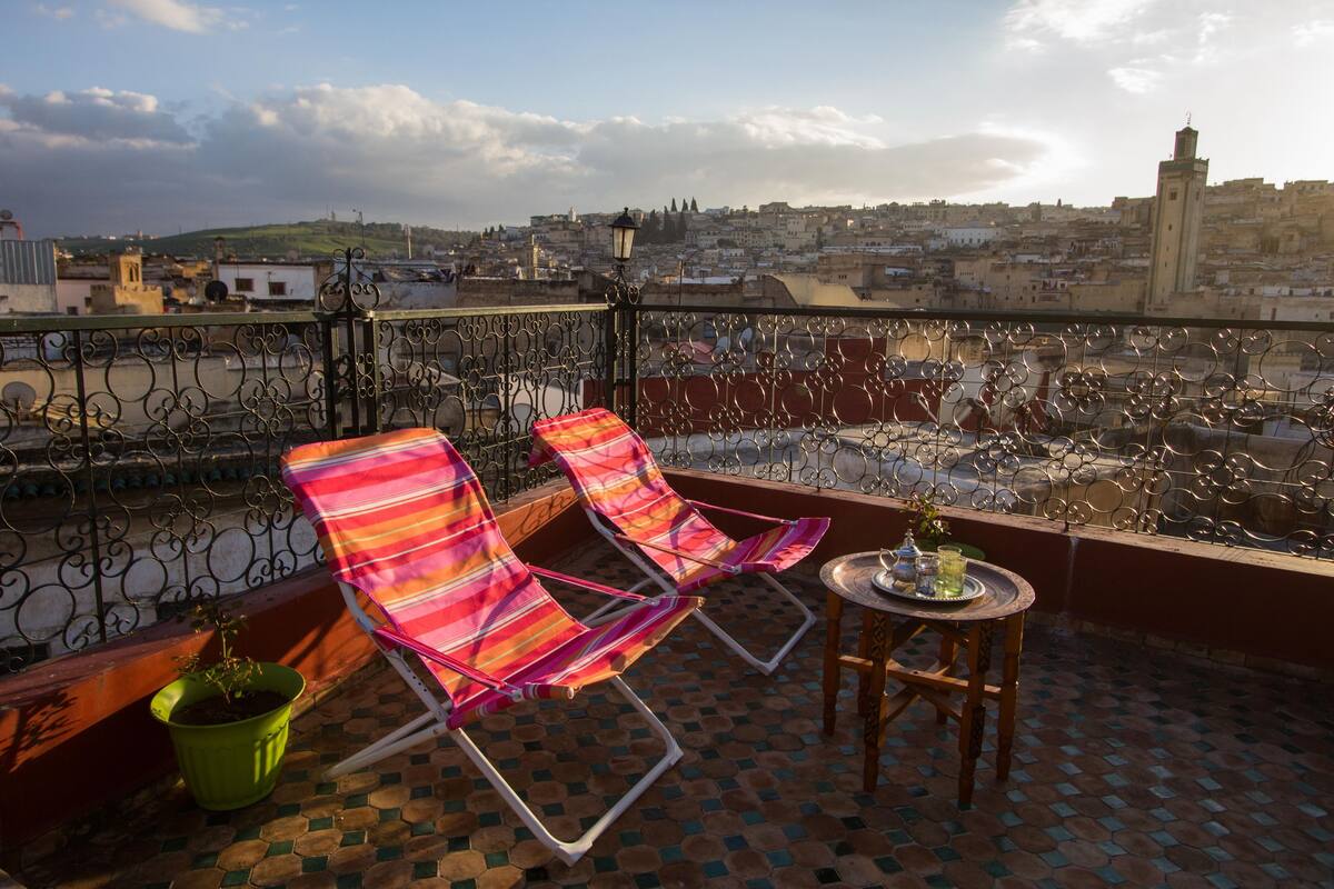 A balcony with two striped lounge chairs, a small table with a tray, and a potted plant.