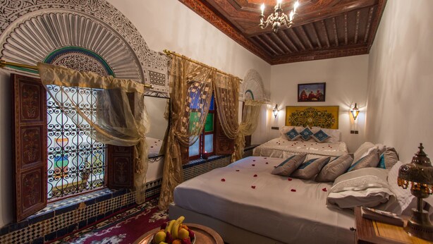 A traditional room with a bed, a decorative window, a chandelier, and a wall-mounted lamp. - Riad El Bacha (Fes)