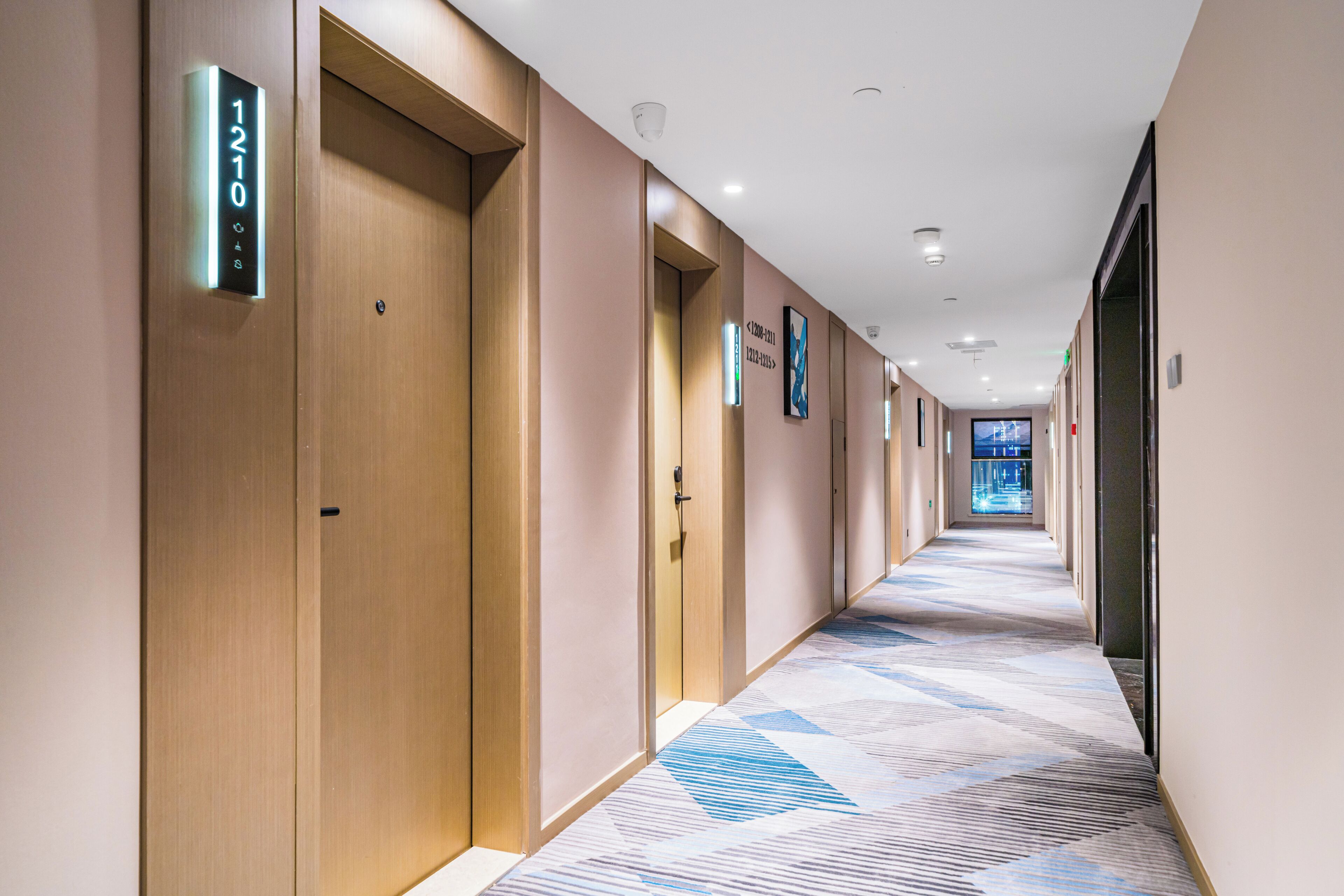 A modern hotel corridor with wooden doors, numbered room signs, and a patterned carpet.