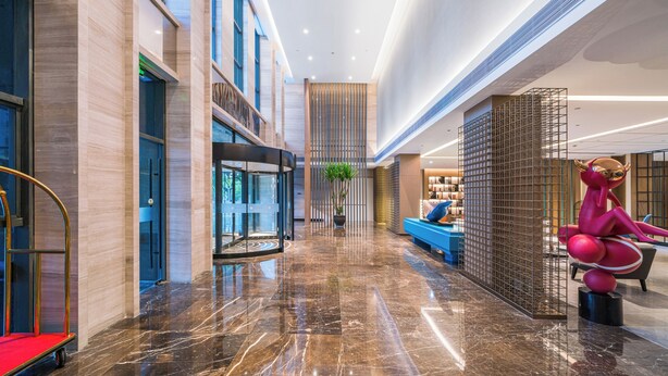 A spacious lobby with a polished marble floor, a reception area with a blue sofa, and a unique pink sculpture. - Hangzhou Wassim Resorts Hotel  (Hangzhou)