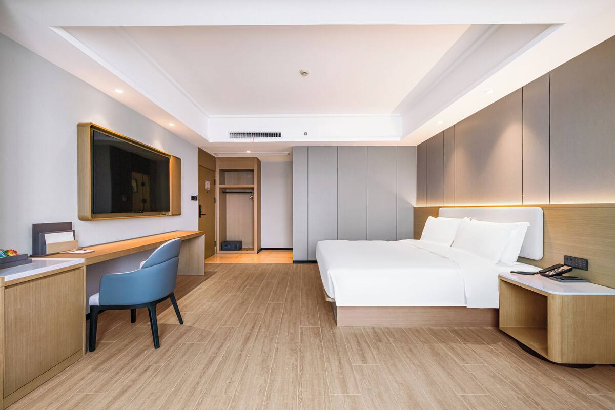 A modern hotel room with a bed, desk, chair, and a large mirror on the wall.