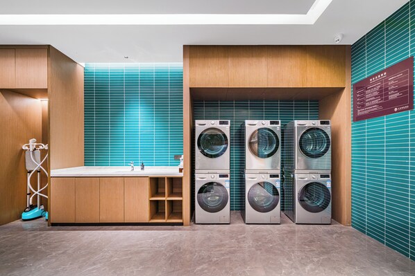 A modern laundry room with a sink, wooden cabinets, and stacked washing machines. - Hangzhou Wassim Resorts Hotel (Hangzhou)