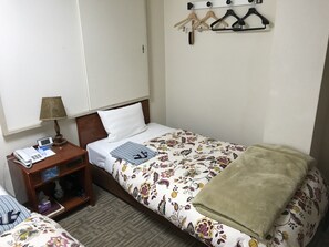 Een hotelkamer met een bed, nachtkastje met een lamp, een telefoon, een klein plankje met toiletartikelen en een kapstok aan de muur.