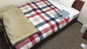Ein Einzelbett mit einer karierten Bettdecke, einer beigen Tagesdecke und einem gemusterten Kopfkissen.