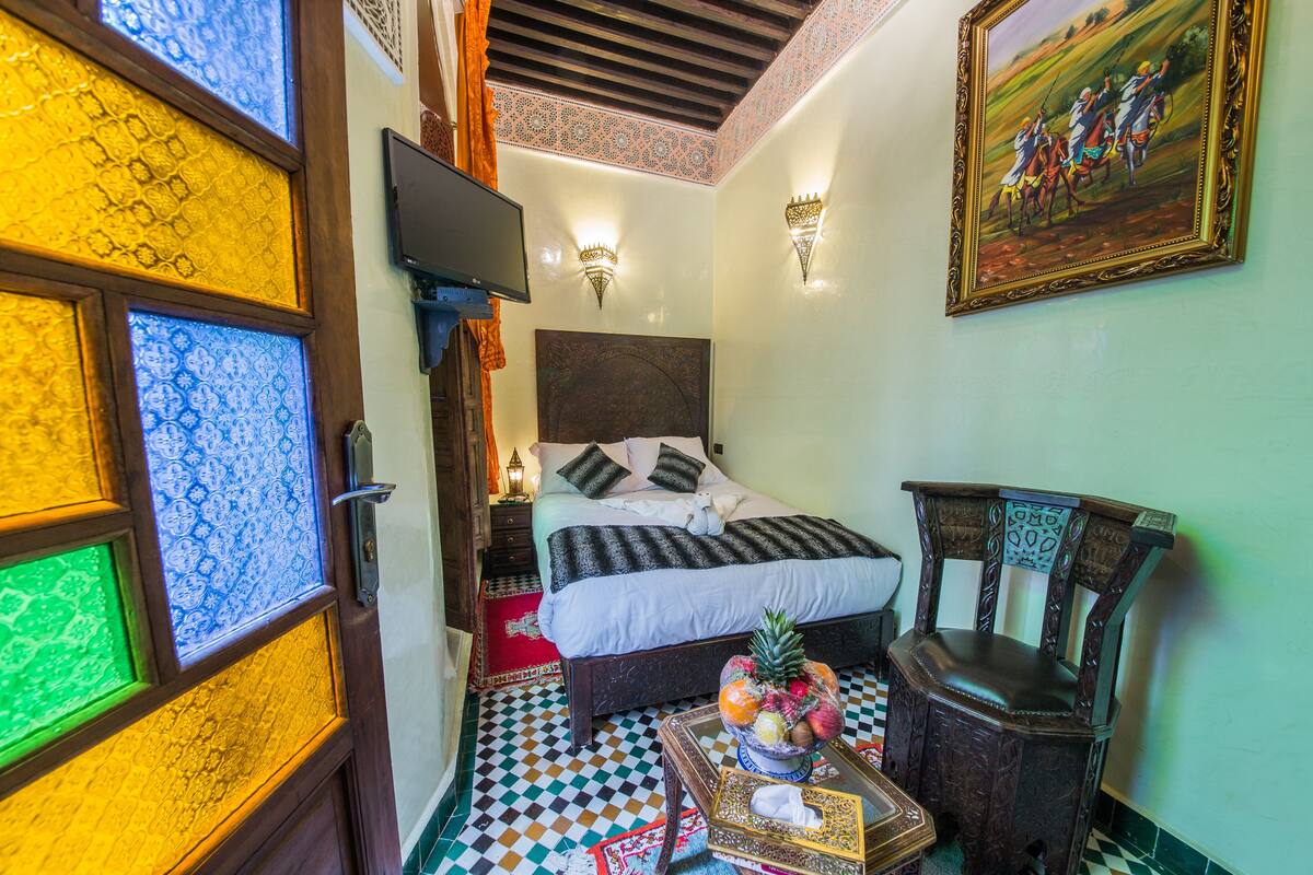 A room with a bed, a chair, a television, and a painting on the wall.
