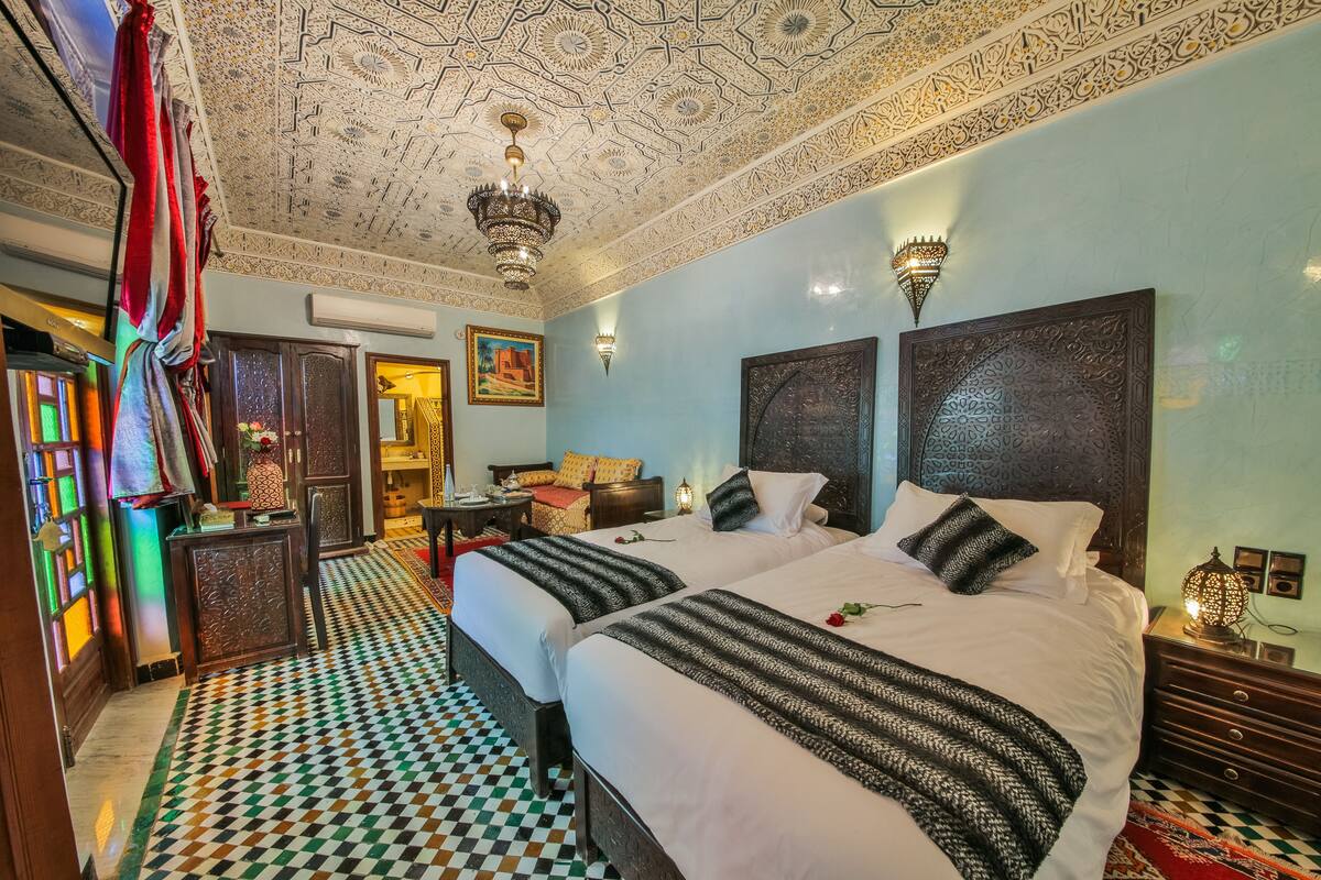 A hotel room with two beds, a patterned floor, and ornate ceiling designs.