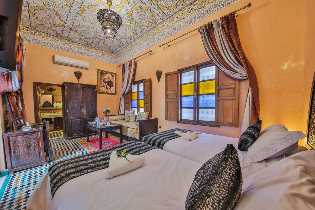 A traditional room with a patterned ceiling, a bed with multiple pillows, a wooden cabinet, and a small table.