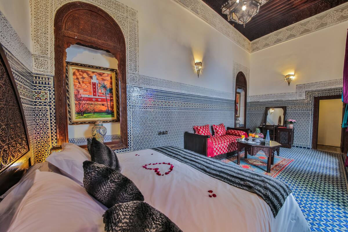 A room with a large bed, a sofa, and a small table with a vase.