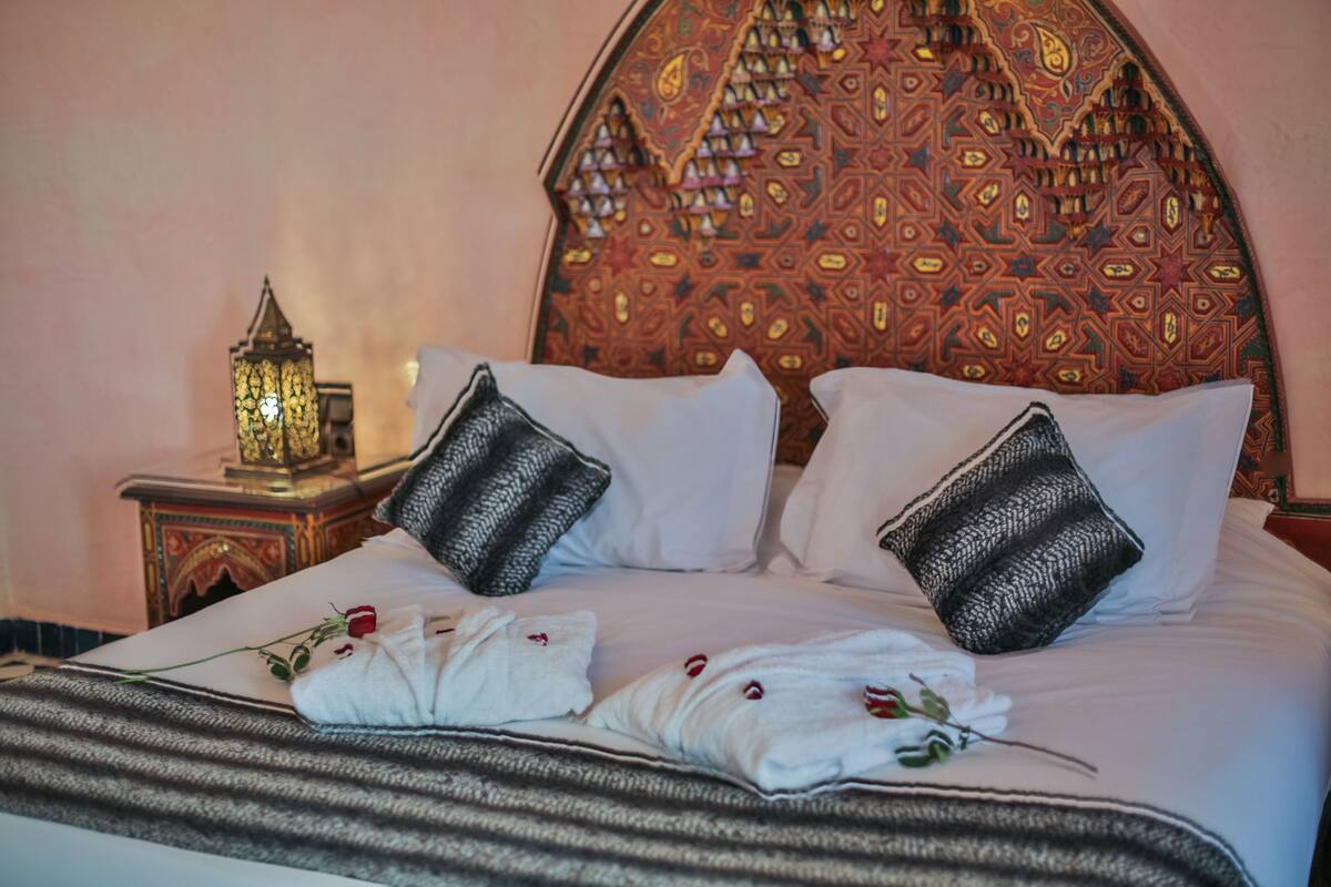 A bed with white linens, two black pillows, a striped blanket, and a single rose.