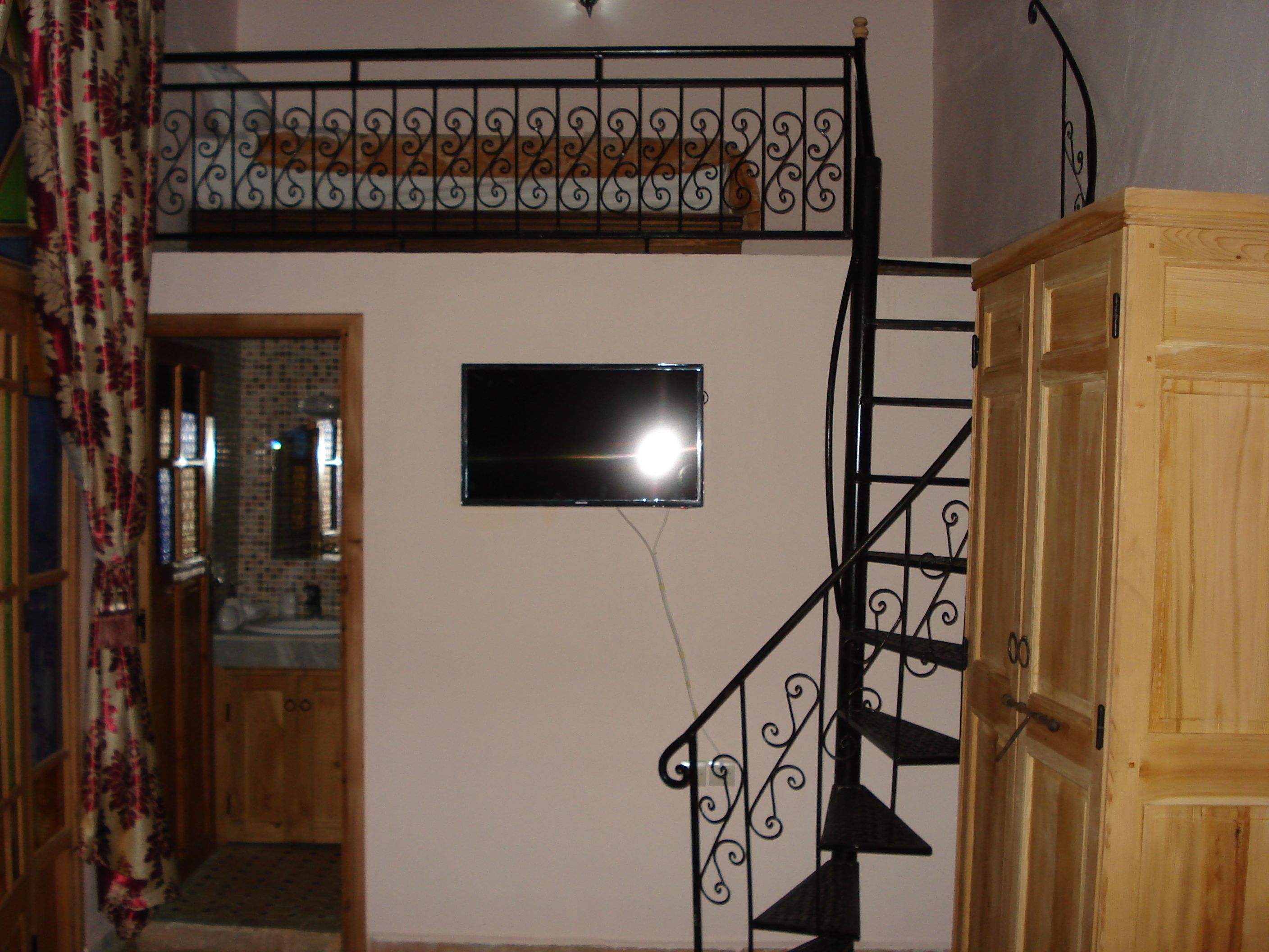 Ein Zimmer mit einer Holztreppe, einem an der Wand montierten Fernseher und einem Holzschrank.