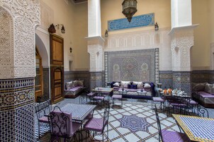 Um interior marroquino com trabalhos em azulejos detalhados, um sofá, mesas e cadeiras.