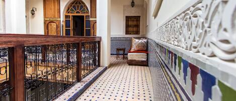 A corridor with a tiled floor, a wooden railing, and a patterned wall.