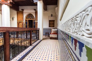Um corredor com piso de azulejos, corrimão de madeira e papel de parede estampado.