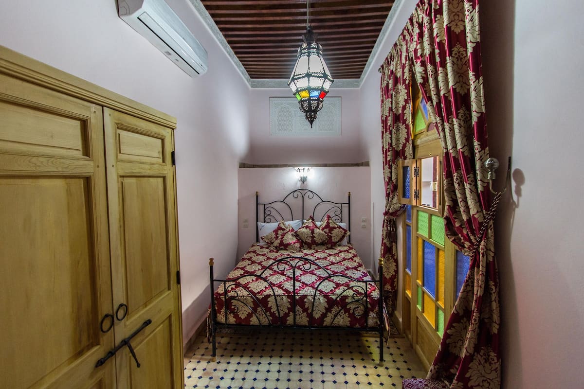 A bedroom with a bed, wooden wardrobe, and a ceiling fan.