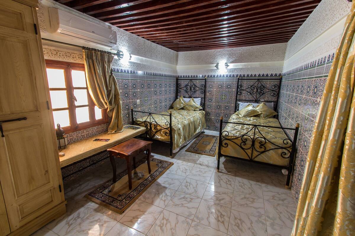 A room with two beds, a wooden desk, and a window with curtains.
