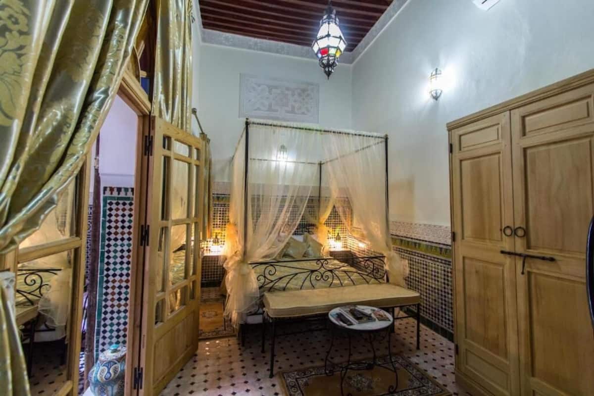 A room with a bed under a canopy, a small table, a cabinet, and a decorative wall.