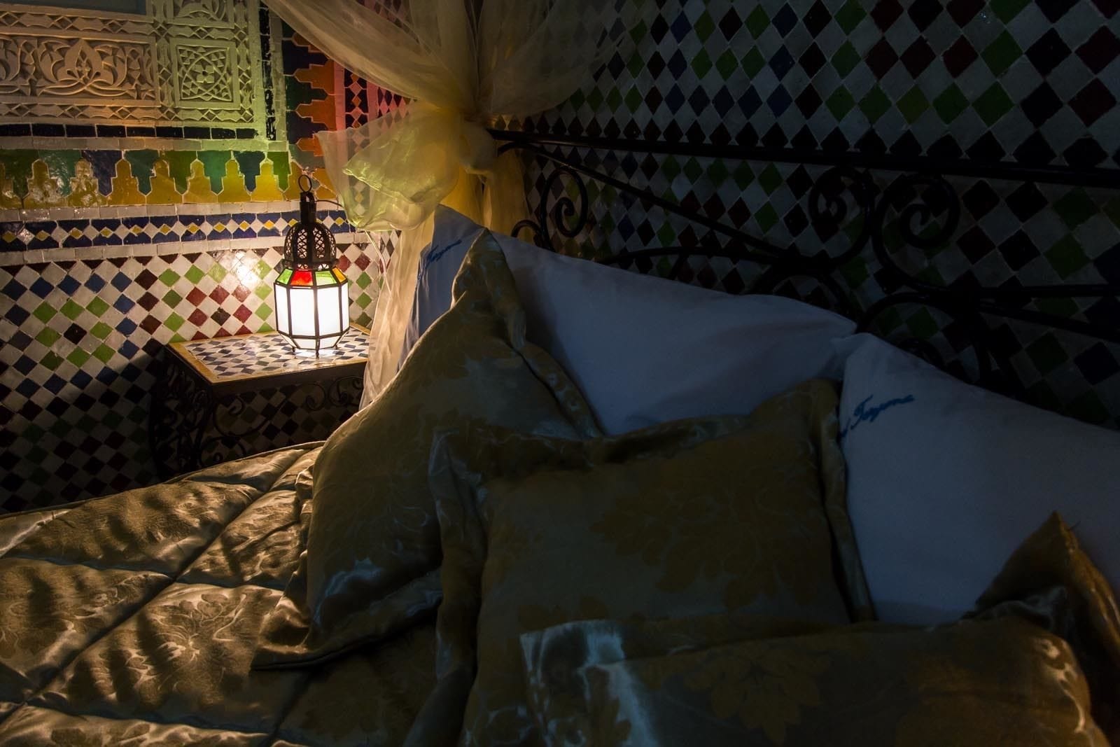 A bed with patterned pillows and a nightstand with a decorative lantern.