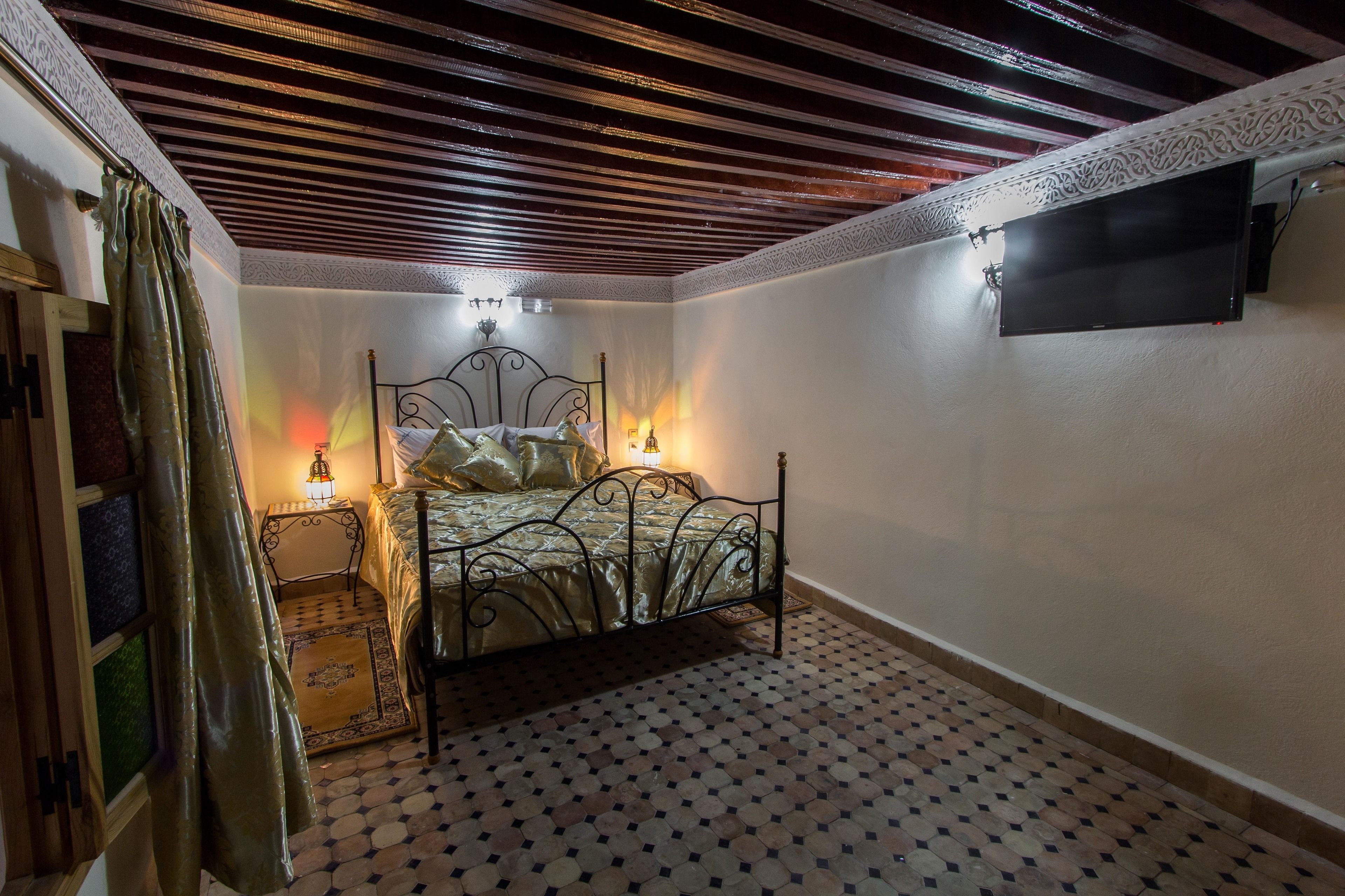 Un dormitorio con cama, mesita de noche, televisor montado en la pared y piso estampado.