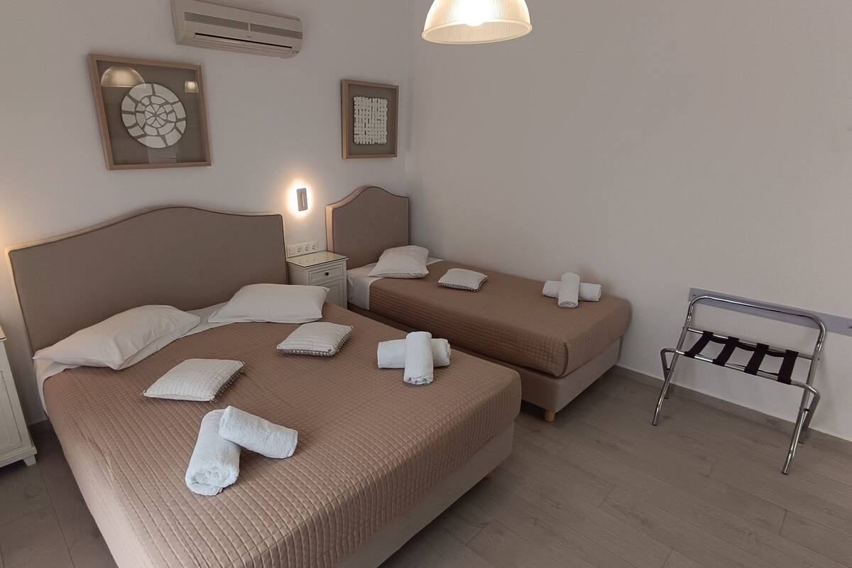 Habitación de hotel con dos camas, cada una con cabecero, mesitas de noche y lámparas. Se observan obras de arte enmarcadas en las paredes y un perchero metálico con toallas.