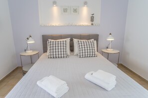 Uma cama bem arrumada com almofadas xadrez, duas mesas de cabeceira com luminárias e uma prateleira na parede com objetos decorativos.
