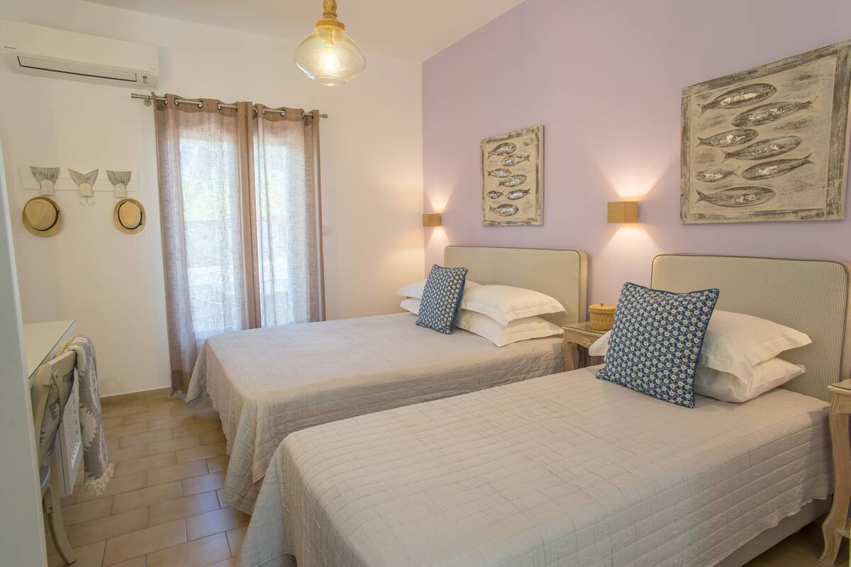 Un dormitorio con dos camas, una ventana con cortinas, luces fijadas a la pared y obras de arte.
