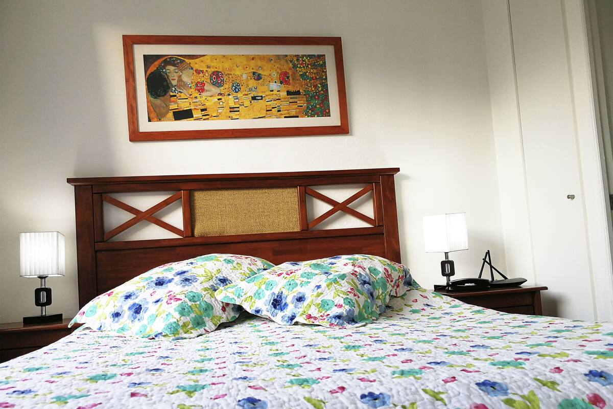 A neatly made bed with a floral quilt, a wooden headboard, and a framed painting above.