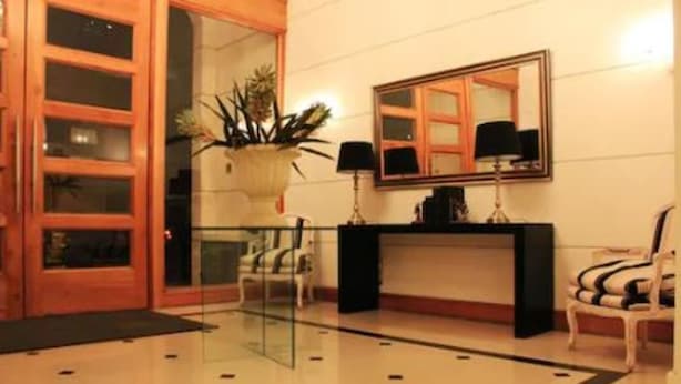A lobby with a glass partition, a reception desk, a potted plant, and a chair. - Amistar Plaza París (Santiago)
