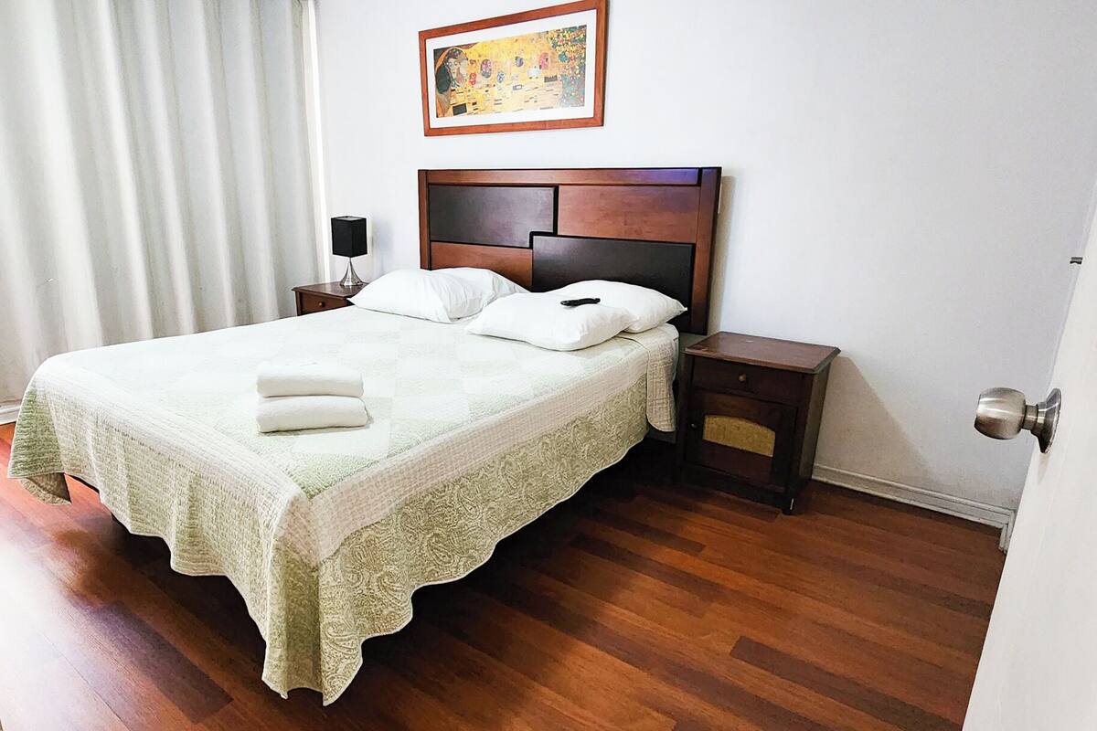 A neatly made bed with a wooden headboard, a bedside table with a lamp, and a framed picture on the wall.