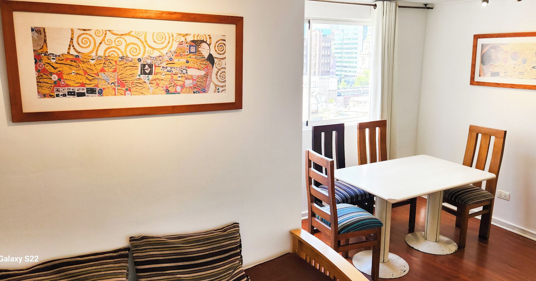 Un espace repas comprenant une table et des chaises, un banc et deux œuvres d’art encadrées accrochées aux murs.