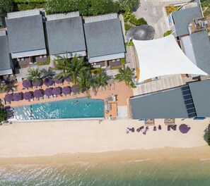 Vista aérea de um resort com piscina, praia e vários quartos de hotel.